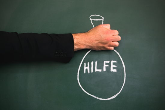 Sack mit Aufschrift „Hilfe“ mit Kreide auf Tafel, gehalten von einer Hand